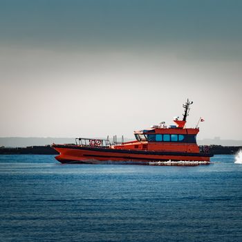 Red pilot ship moving at speed past the breakwater dam