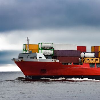 Red cargo container ship's bow in cloudy day