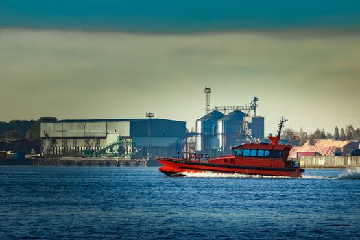 Red pilot ship moving past the factory in Latvia