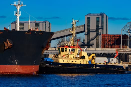 Black cargo ship mooring at the port with tug ship support