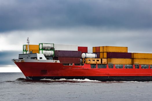 Red cargo container ship's bow in cloudy day