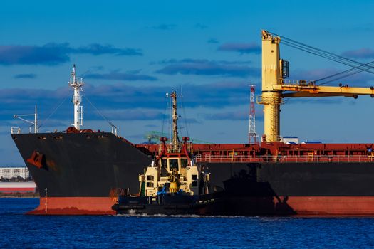 Black cargo ship mooring at the port with tug ship support