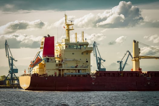 Red cargo ship's stern against port cranes