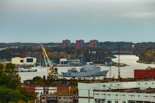 Military ship sailing past the cargo port in Riga, Latvia