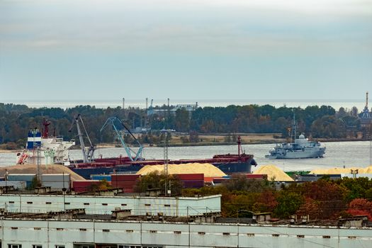 Military ship sailing past the cargo port in Riga, Latvia