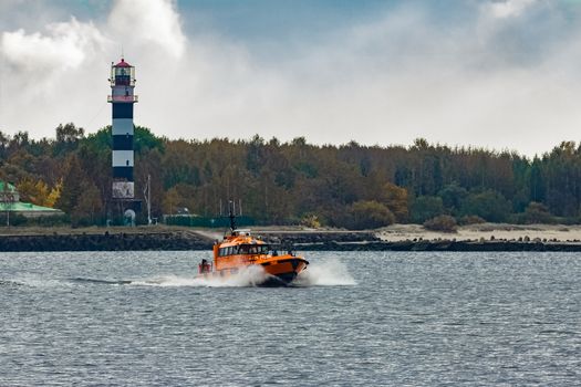 Orange pilot ship moving at speed past the lighthouse in Riga