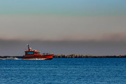 Red pilot ship moving past the breakwater dam in Riga, Europe