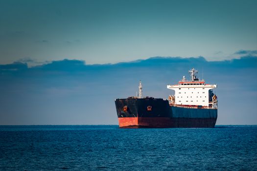 Black cargo ship moving in still Baltic sea water. Riga, Europe