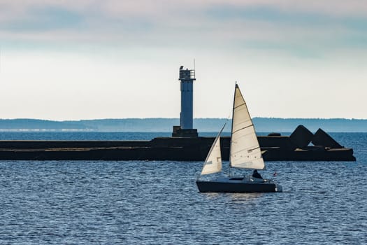 Small sailboat traveling past the lighthouse in sunny day