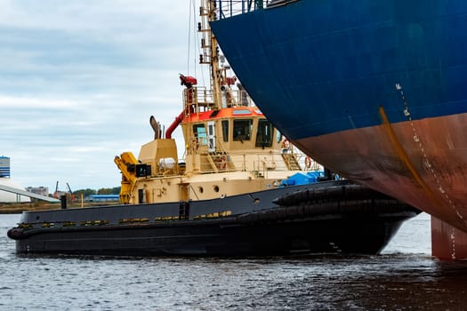 Tug ship towing blue bulk carrier in the port of Riga