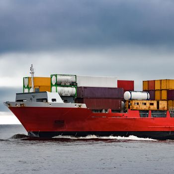 Red cargo container ship's bow in cloudy day