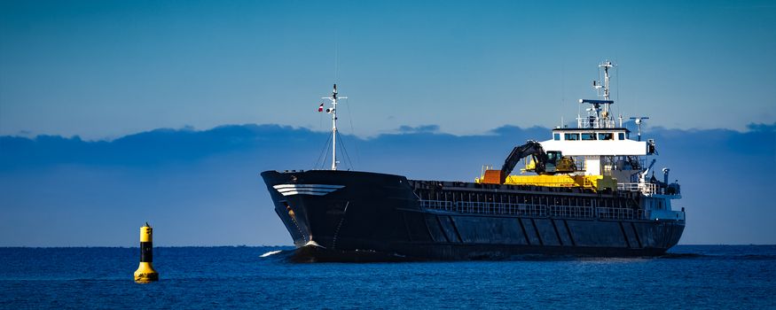 Black cargo ship with long reach excavator moving by baltic sea