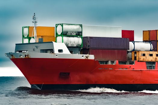 Red cargo container ship's bow in cloudy day