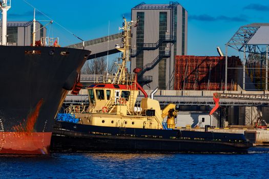 Black cargo ship mooring at the port with tug ship support