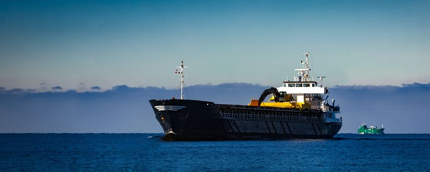 Black cargo ship with long reach excavator moving by baltic sea