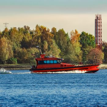 Red pilot ship moving past the autumn trees in Europe