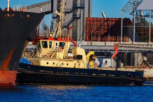 Black cargo ship mooring at the port with tug ship support