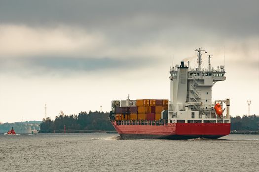 Red cargo container ship entering the port of Riga in cloudy day