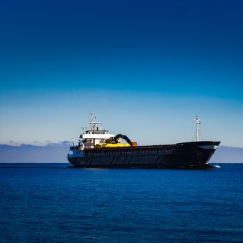 Black cargo ship with long reach excavator moving by baltic sea