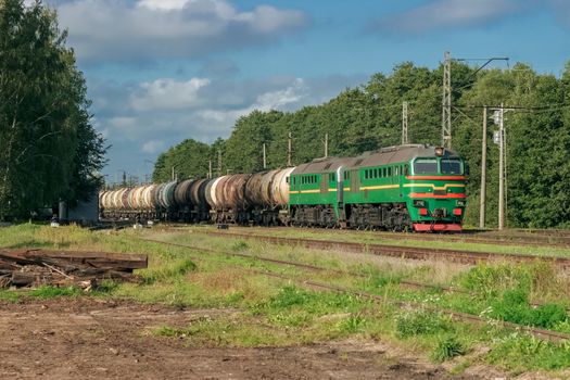 Freight train with tank wagons in forest. Green cargo locomotive