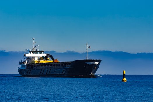 Black cargo ship with long reach excavator moving by baltic sea