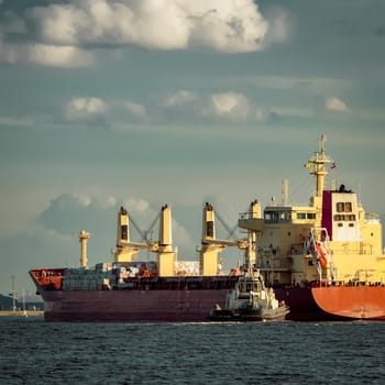 Red cargo ship and the tug ship towing it to the port