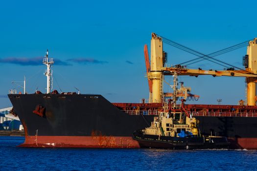 Black cargo ship mooring at the port with tug ship support