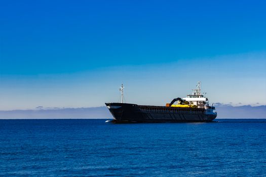 Black cargo ship with long reach excavator moving by baltic sea