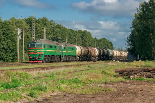 Freight train with tank wagons in forest. Green cargo locomotive