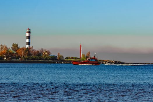 Red pilot ship moving past the lighthouse in Riga