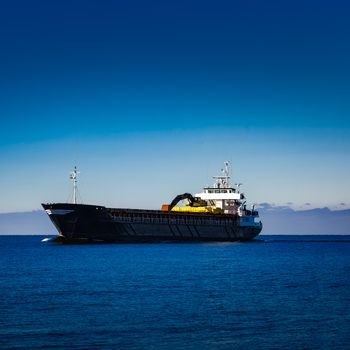 Black cargo ship with long reach excavator moving by baltic sea