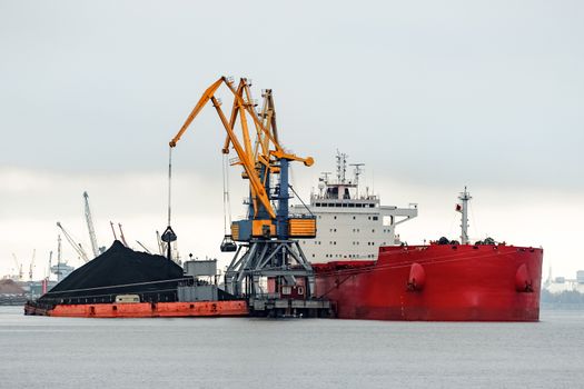 Large red cargo ship loading with a coal in the port