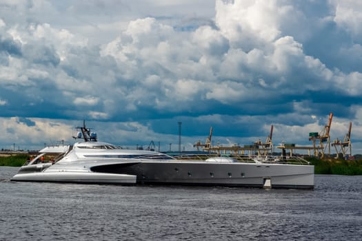 Large silver trimaran. Luxury yacht sailing by the river in Riga