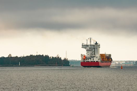 Red cargo container ship entering the port of Riga in cloudy day