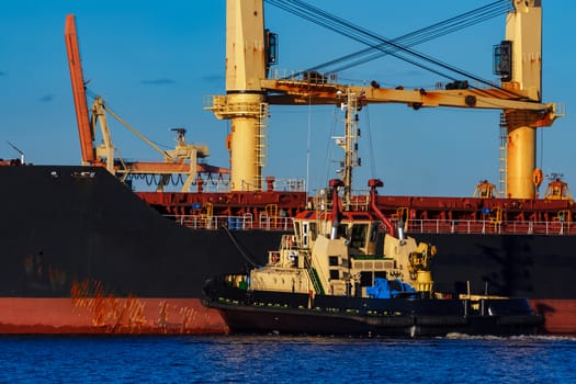 Black cargo ship mooring at the port with tug ship support