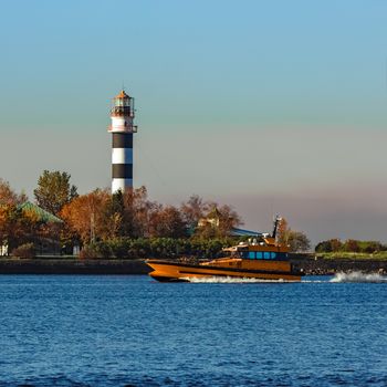 Orange pilot ship sailing past the lighthouse in Europe