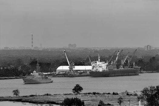 Military ship sailing past the cargo port in Latvia. Monochrome
