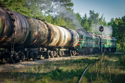 Freight train with tank wagons in forest. Green cargo locomotive