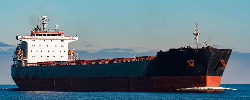 Black cargo ship moving in still Baltic sea water. Riga, Europe