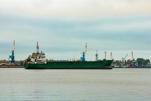 Green cargo ship moving to the port in cloudy day