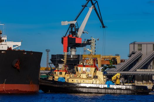 Black cargo ship mooring at the port with tug ship support