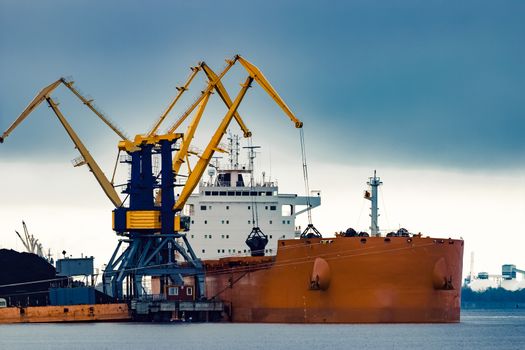 Large orange cargo ship loading with a coal in the port