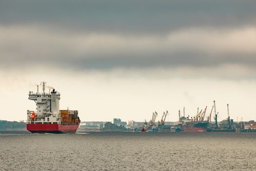 Red cargo container ship entering the port of Riga in cloudy day