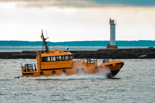 Orange pilot ship moving at speed past the lighthouse in Riga