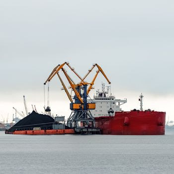 Large red cargo ship loading with a coal in the port