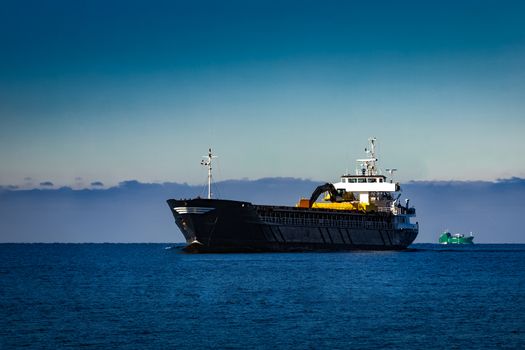 Black cargo ship with long reach excavator moving by baltic sea