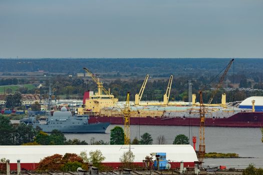 Military ship sailing past the cargo port in Riga, Latvia