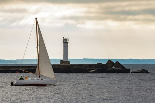 White sailboat traveling past the lighthouse in Riga