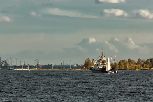 Tug ship and sailboat are coming to port of Riga, Daugava river