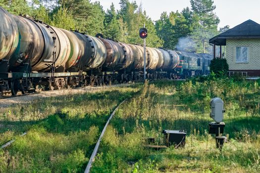 Freight train with tank wagons in forest. Green cargo locomotive